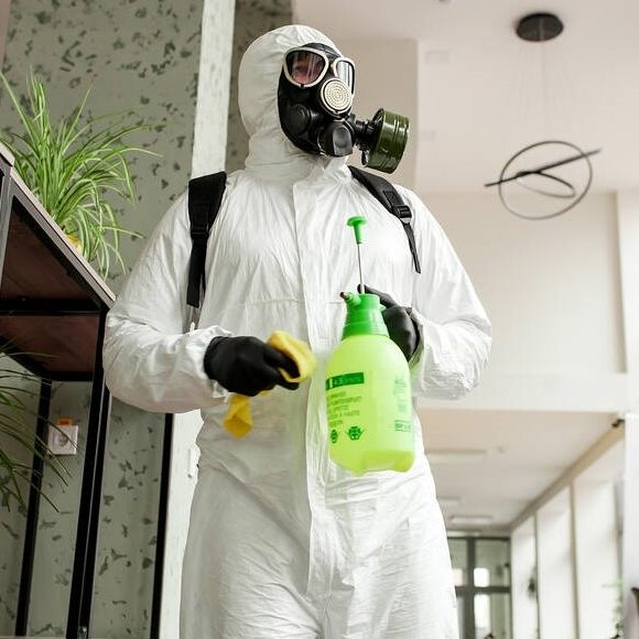 A man in protective equipment disinfects with a sprayer in the office. Surface treatment due to coronavirus covid-19 disease. A man in a white suit disinfects the room with a spray gun. Virus pandemic